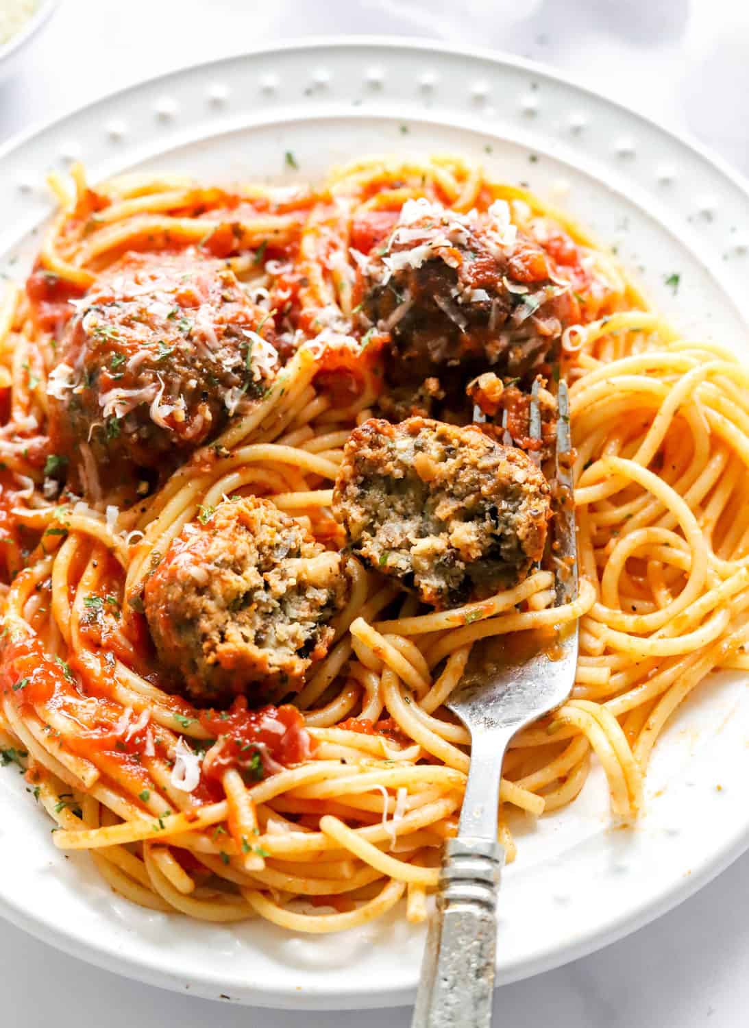 4 meatballs sliced open on a pile of spaghetti with a fork under the meatball on a white plate. 