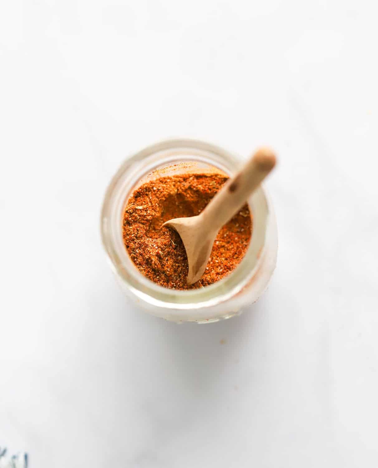 Orange cajun spice blend in a glass spice jar with a wooden spoon in it. 