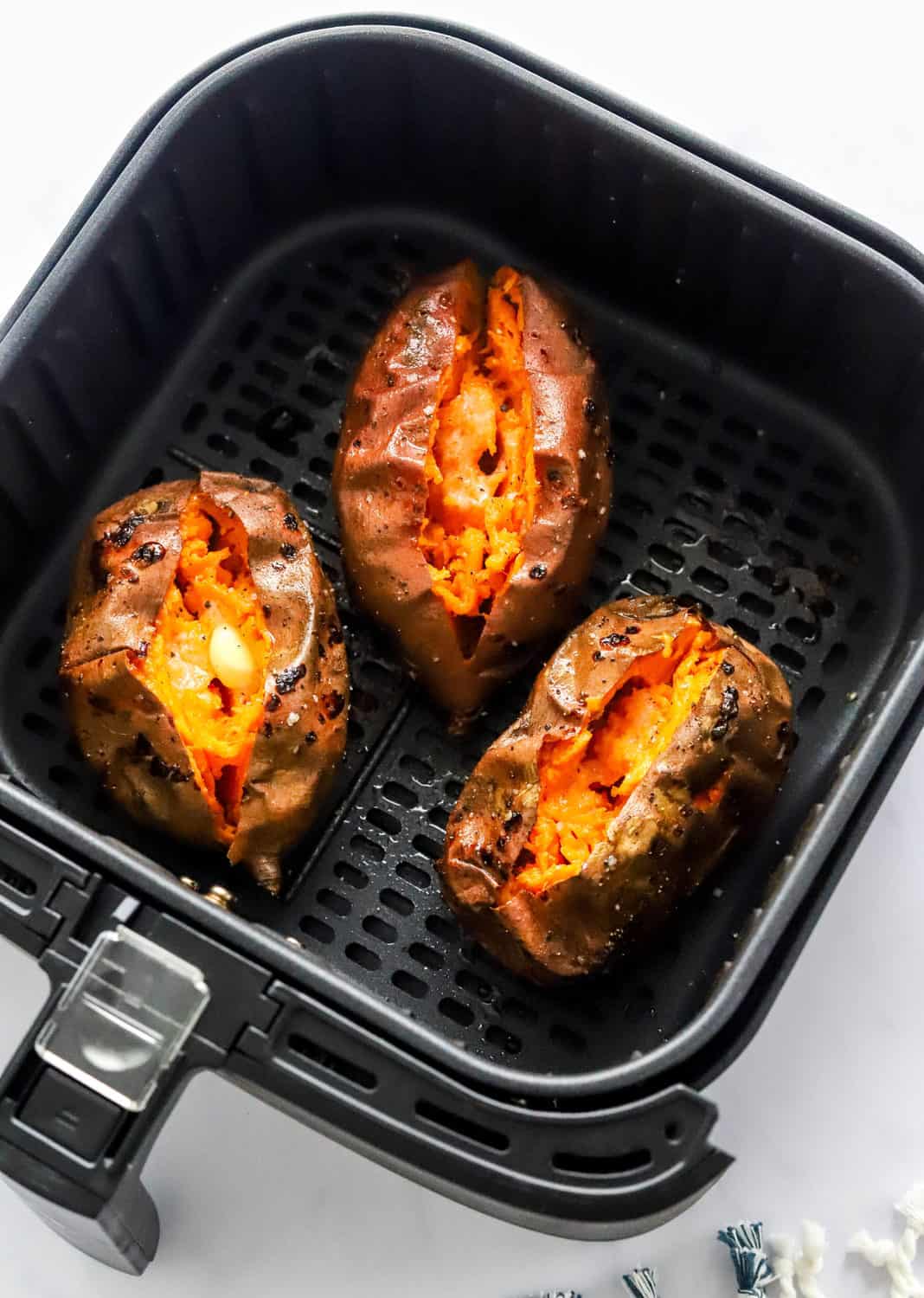 3 whole baked sweet potatoes in a black square air fryer basket. 