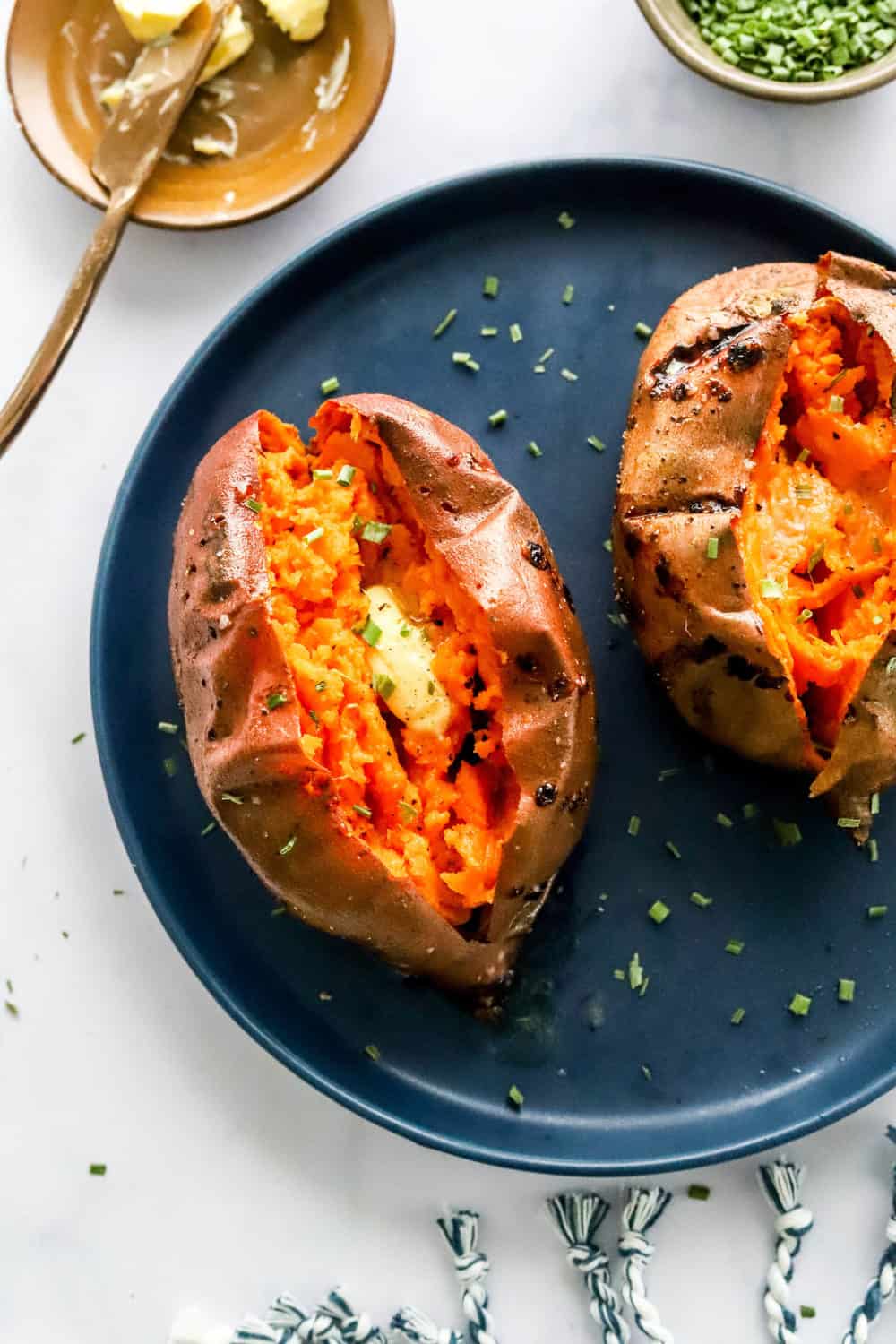 Two air fryer baked sweet potatoes sliced open with butter on them on a blue plate. 