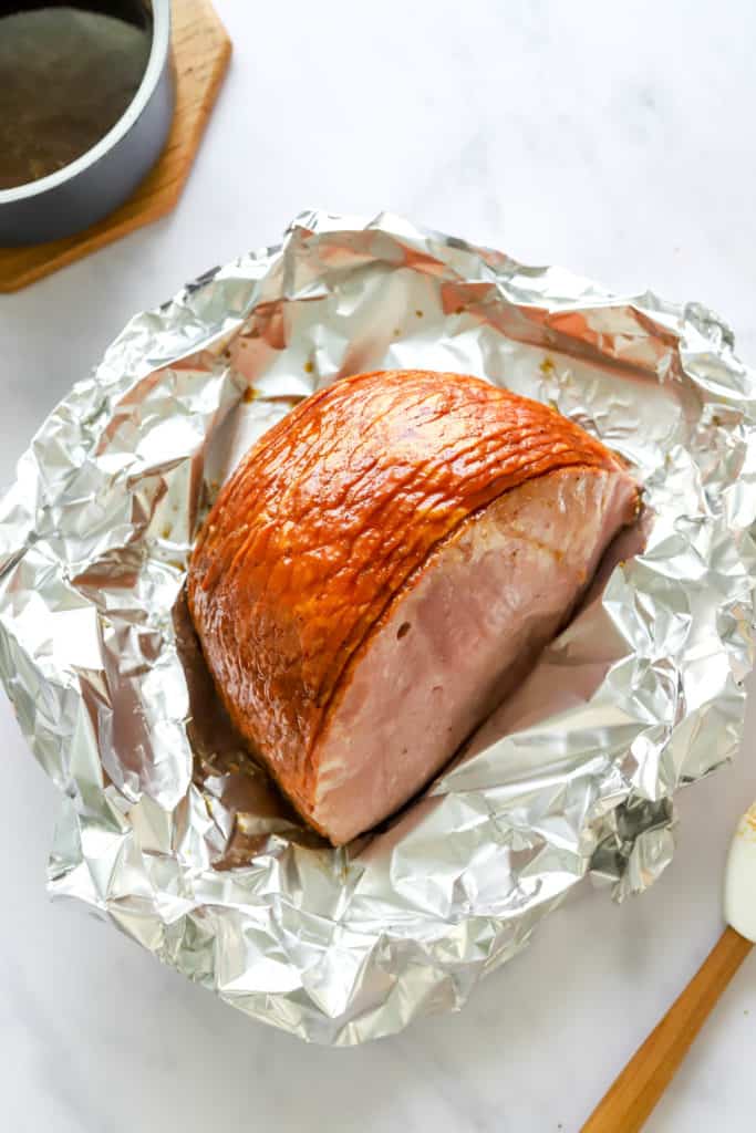 Half a ham on some crinkled foil with a pot of glaze behind it. 