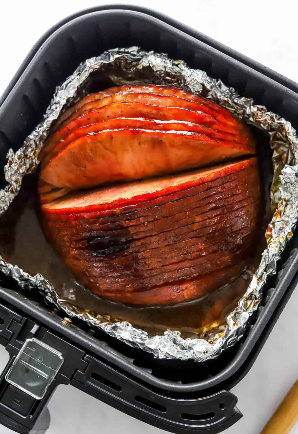 Cooked spiral ham in a foil basket inside a black air fryer basket, 