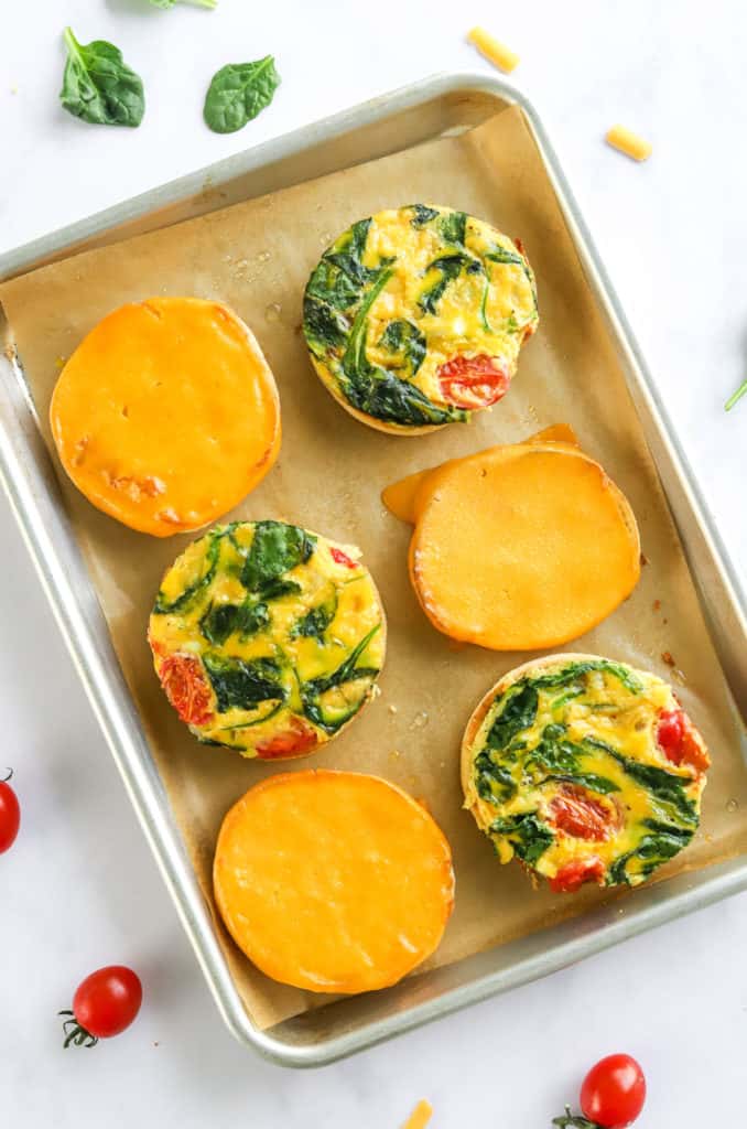 Open faced breakfast egg sandwiches on a baking sheet on top of brown parchment paper. 