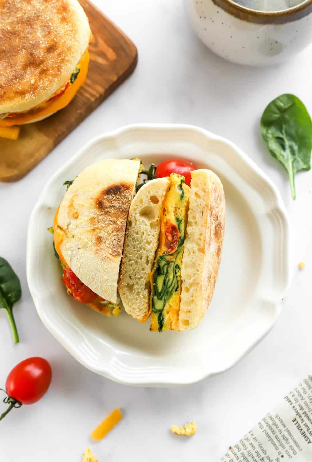 Healthy veggie and egg breakfast sandwich sliced open on a round white plate with more sandwiches behind it. 
