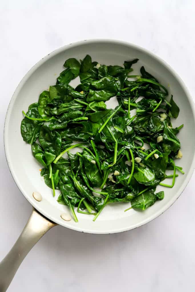 Cooked spinach in a light grey sauté pan.