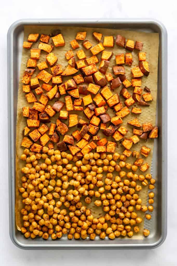 Baking sheet lined with parchment paper with roasted sweet potatoes and crispy chickpeas spread out on it. 