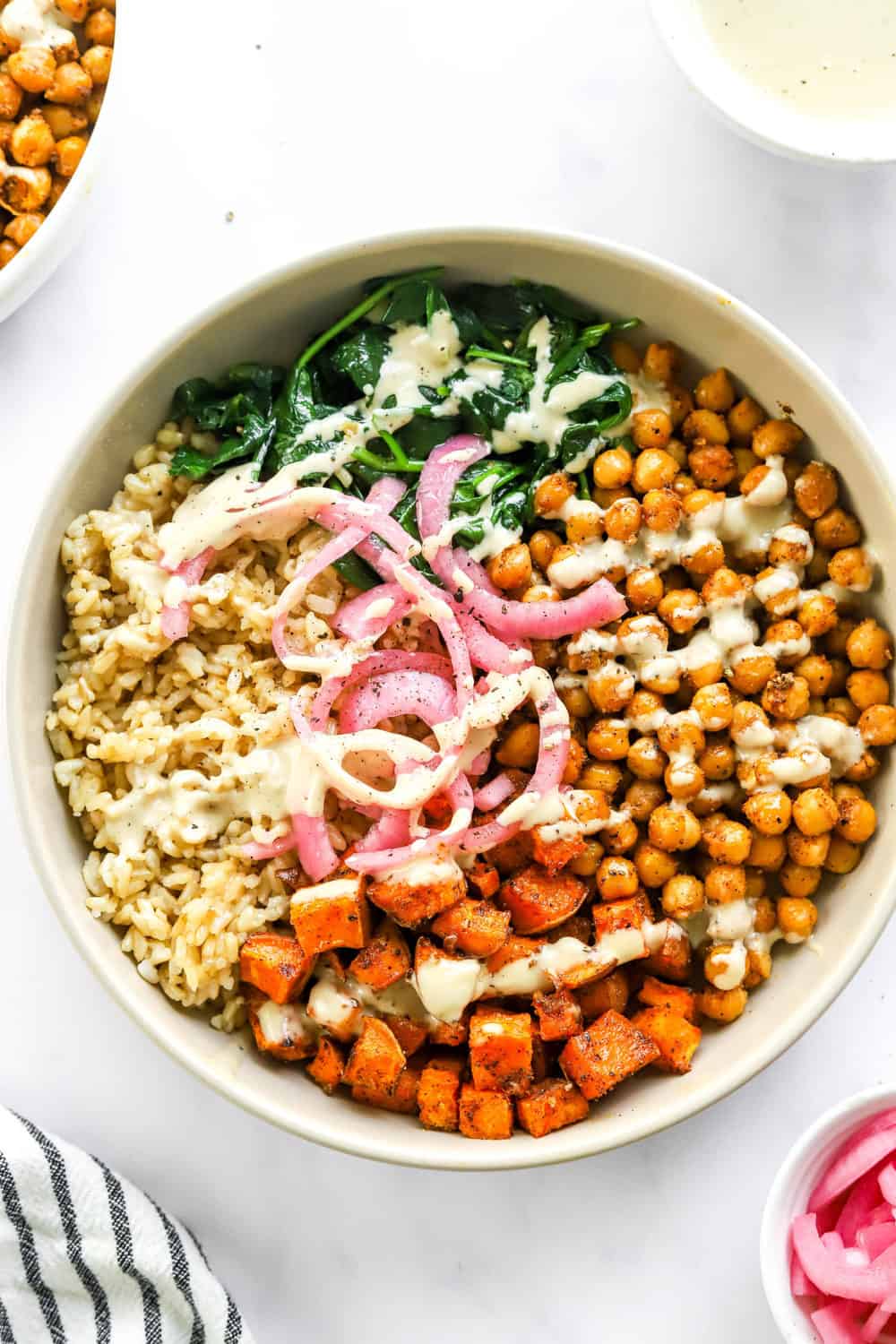 Sweet potato chickpea buddha bowl topped with red onion and white tahini sauce with more red onion in a bowl in front of it. 