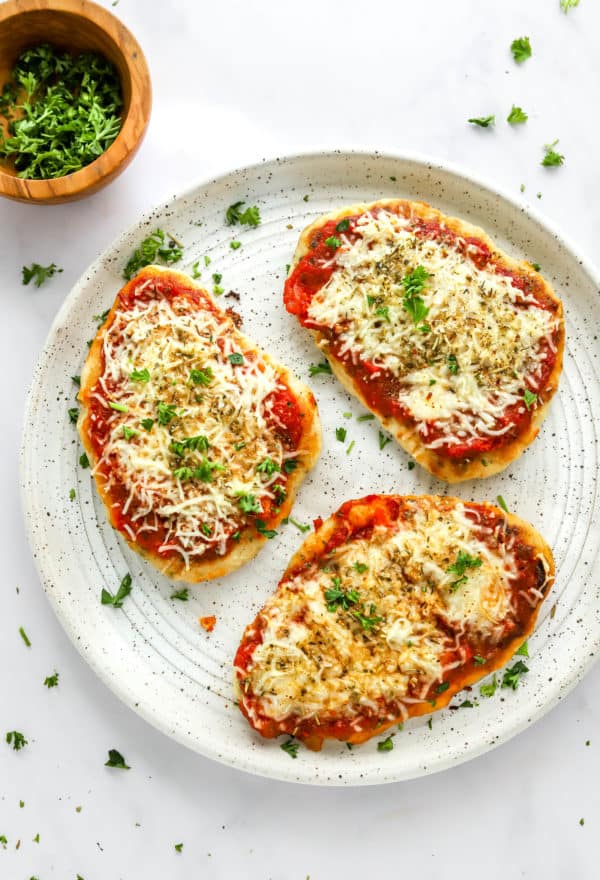 Plate of 3 baked pizzas with pizza sauce, melted cheese sprinkle with green herbs.