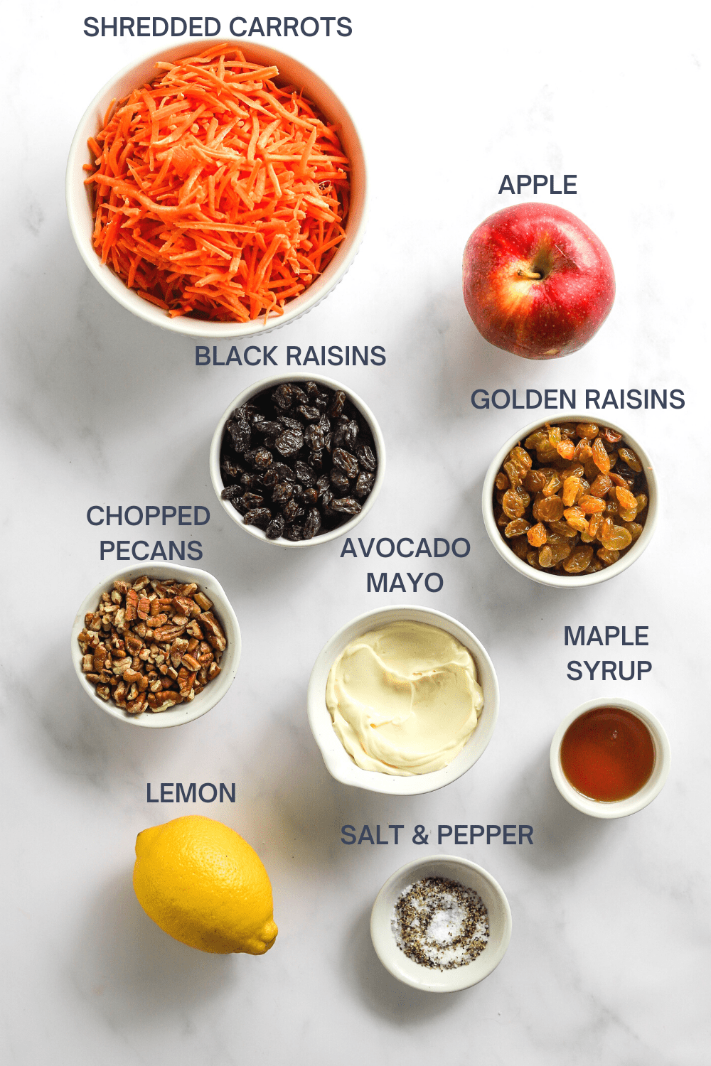 Shredded carrot salad ingredients in white bowls with labels over the top of each ingredient. 