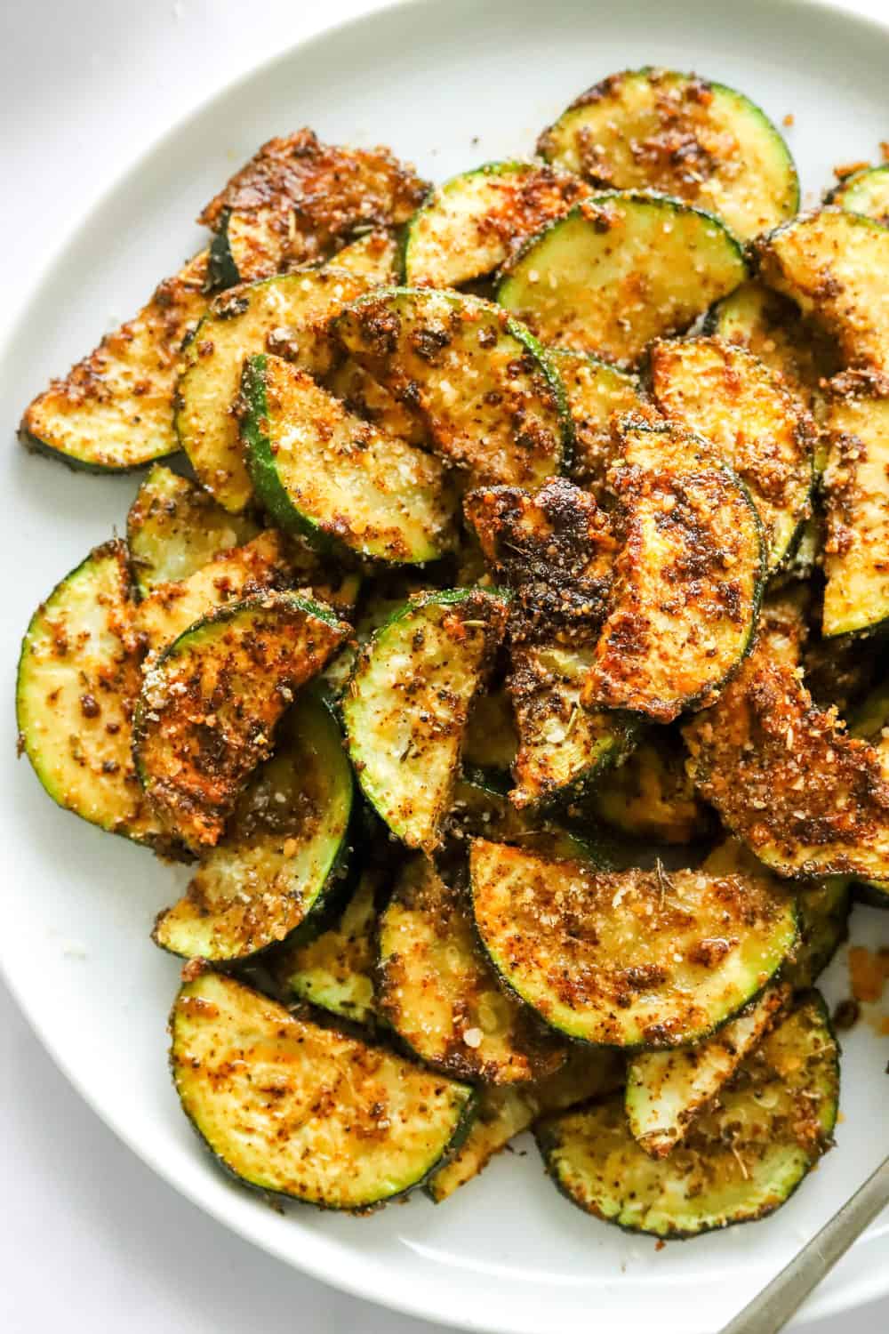 Air fryer zucchini loaded with seasoning on a round white plate. 