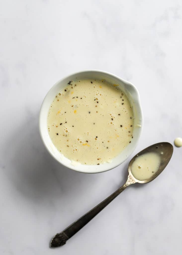 Creamy white dressing with pepper in it in a white bowl with a spoon next to it with more dressing on it. 