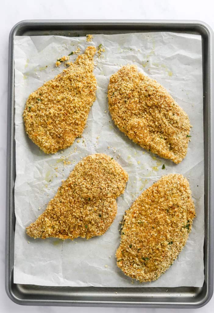 Uncooked coated chicken on a baking sheet on top of white parchment paper. 