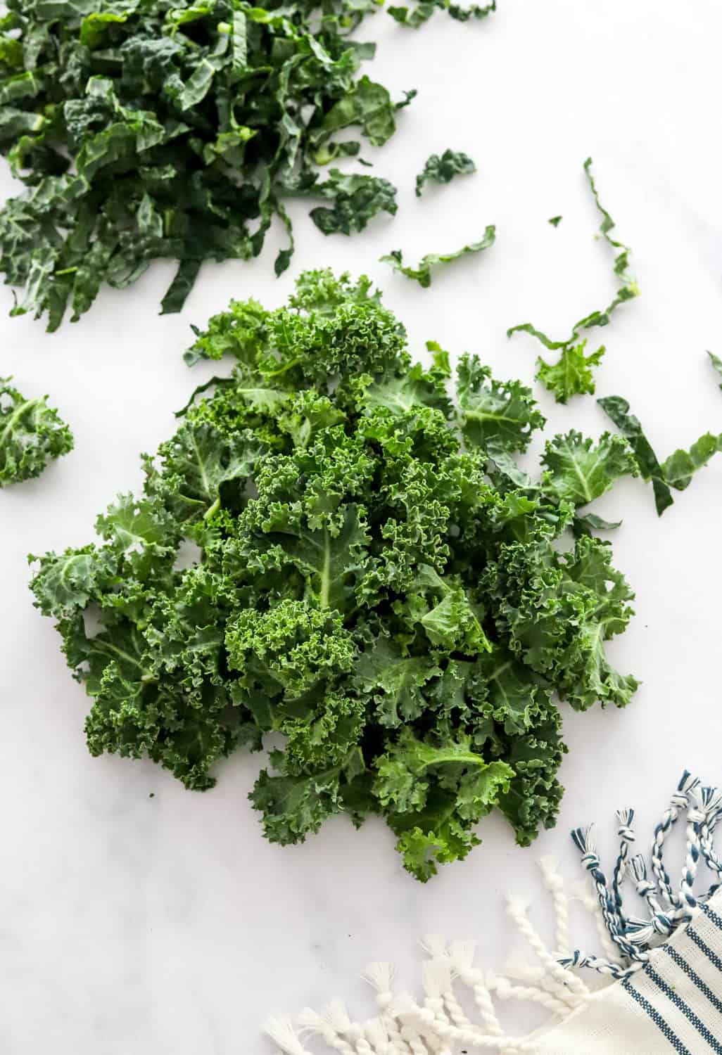 2 piles of chopped fresh kale on a white counter. 