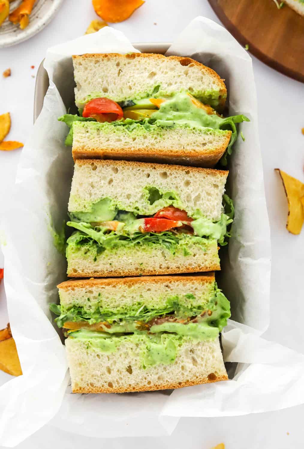 Three sandwiches in a tray on sliced ciabatta bread with a creamy green dressing and veggies in between the slices of bread.