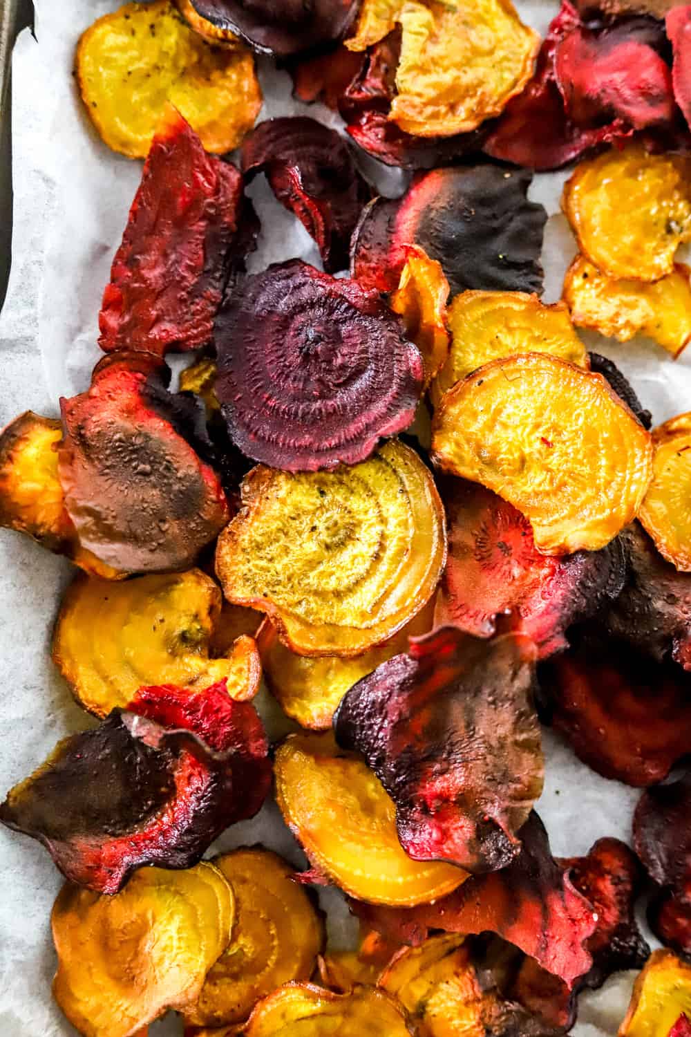 Round and crispy baked red and gold beets piled on top of a white parchment paper lined baking sheet. 