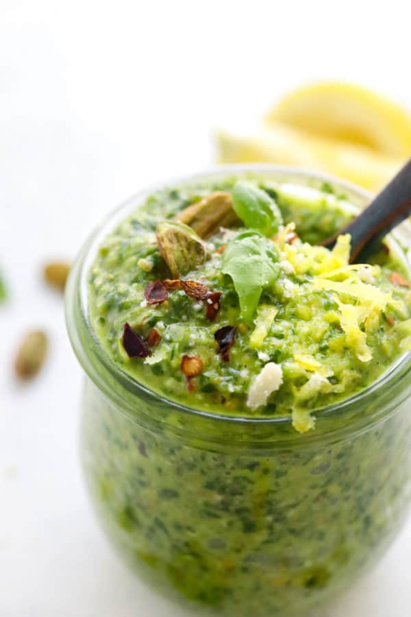 Close up shot of basil pesto in a jar wtj grated lemon zest and red pepper flakes on top of it