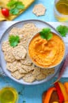 roasted veggies pureed into a dip, piled into a round bowl surrounded bu whole-grain crackers