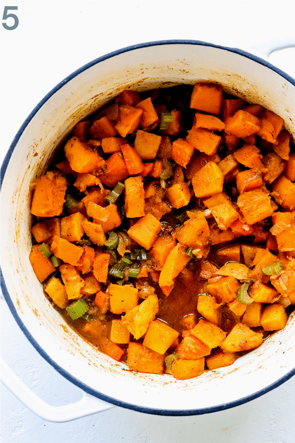 Cooked potato and squash mixed with veggies in a white pot