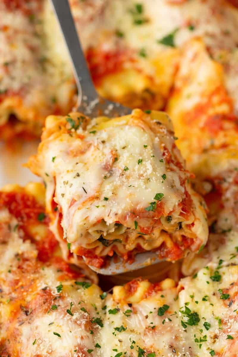 Cheesy lasagna roll on a spatula with more around it. 