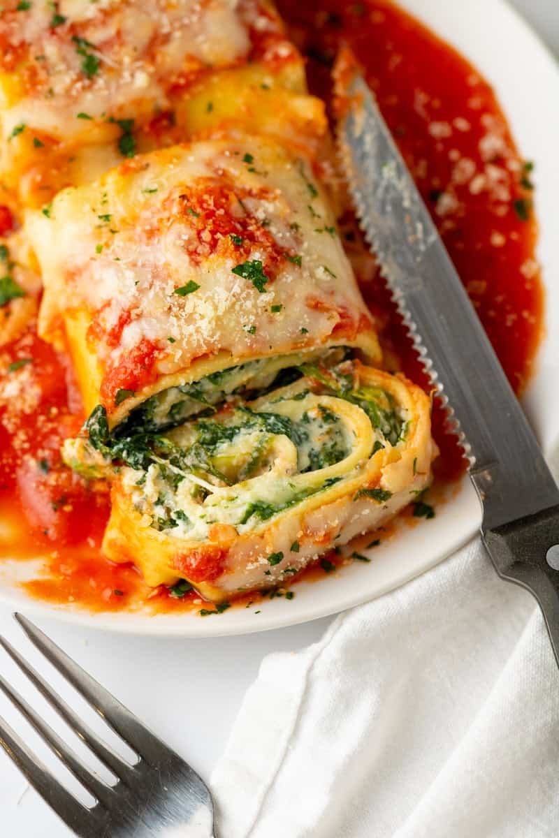 Cut lasagna roll ups with spinach filling on a plate in red sauce. 