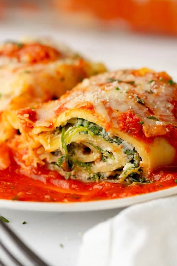 Piece of spinach lasagna on top of tomato sauce on a plate.