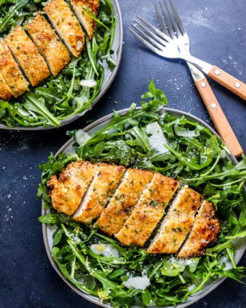 two grey plates filled with arugula salad topped with crispy breaded chicken breast