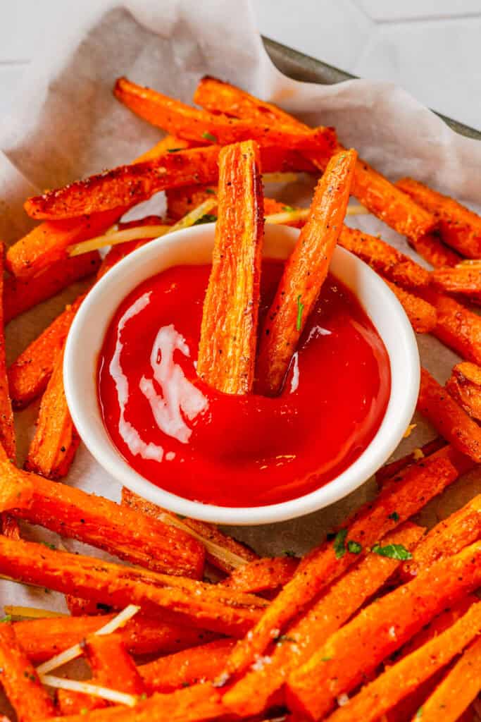 Pan of carrot fries cooke in the air fryer with a bowl of ketch on the pan with the fries.