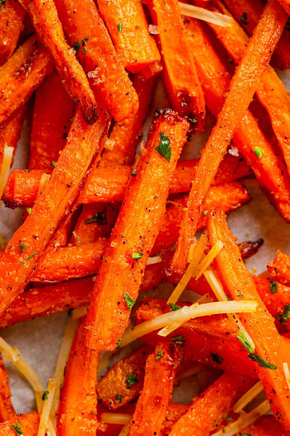Pile of carrot fries with herbs and cheese on them.