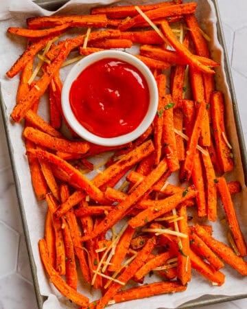 Pan full of air fryer carrot fries with a bowl of ketchup on the pan with it.