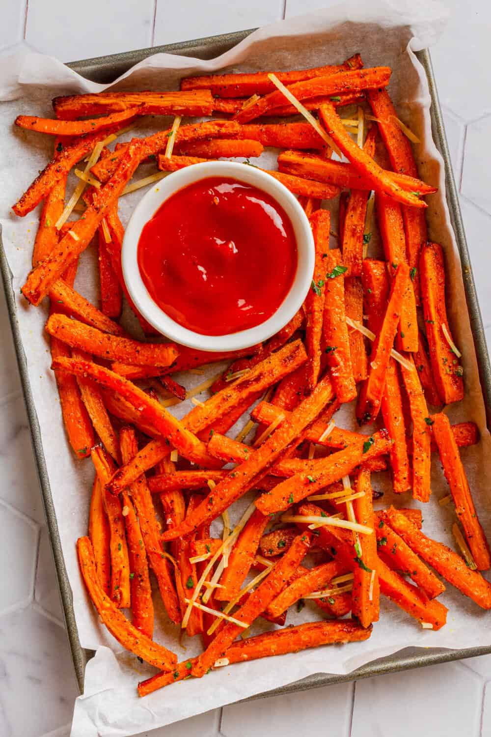 Lined baking pan with cooked air fryer carrot fries with a white bowl of ketchup on the pan with them.
