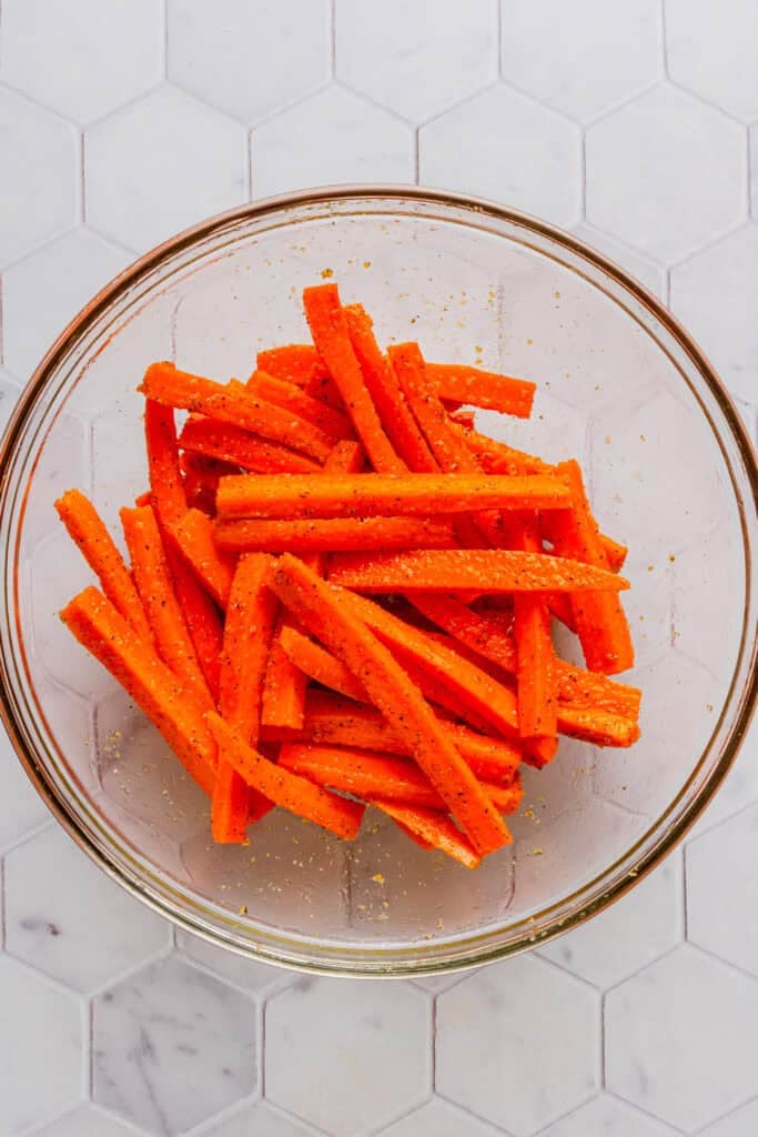 Seasoned carrot sticks in a glass bowl.