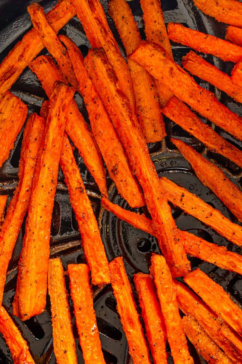 Golden flavorful carrot fries in an air fryer basket.