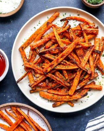 Air Fryer carrot fries on a plate with more fries in front of it and ketchup in a bowl next to it