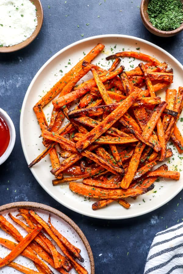 Air Fryer carrot fries on a plate with more fries in front of it and ketchup in a bowl next to it