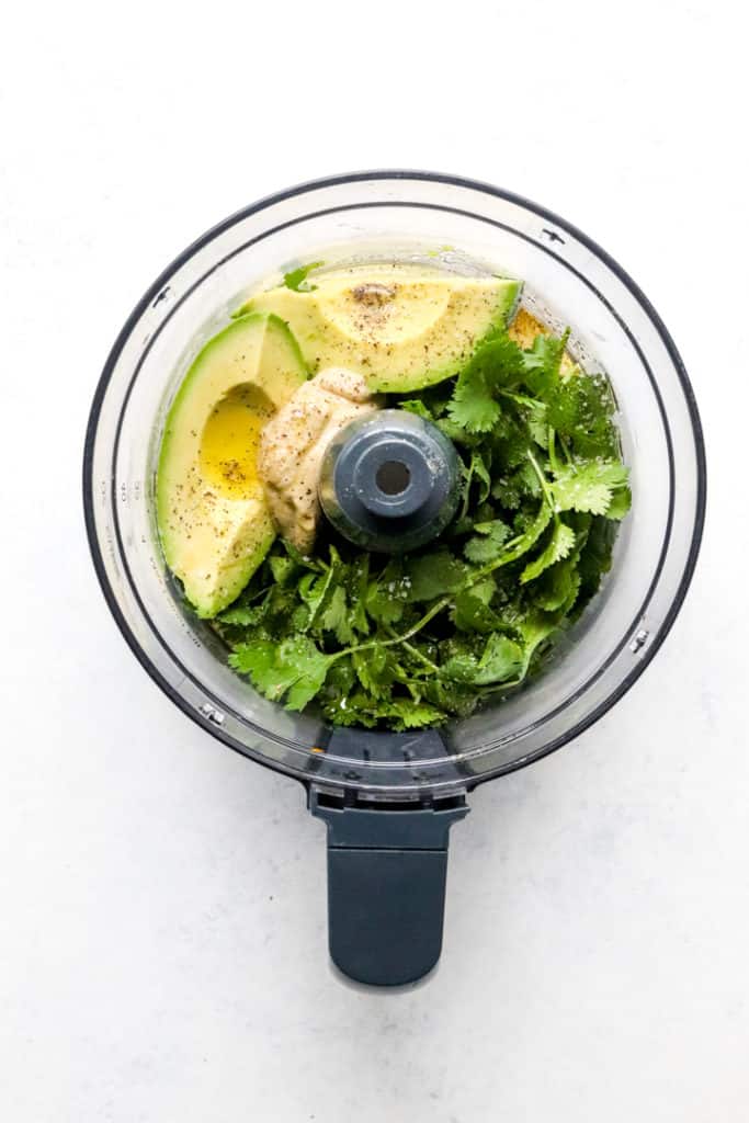 Cilantro, sliced avocado, mustard and olive oil in the bowl of a food processor