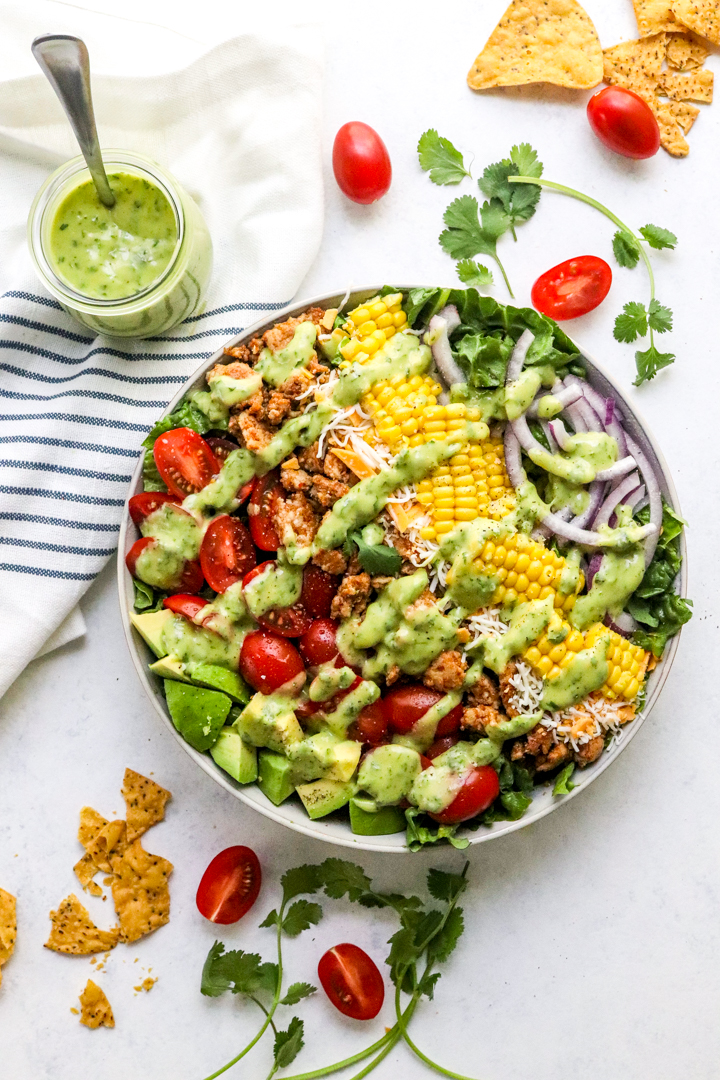 Bow of salad topped with a few drizzles of creamy green cilantro dressing with tomatoes, avocados and corn and chicken in the salad