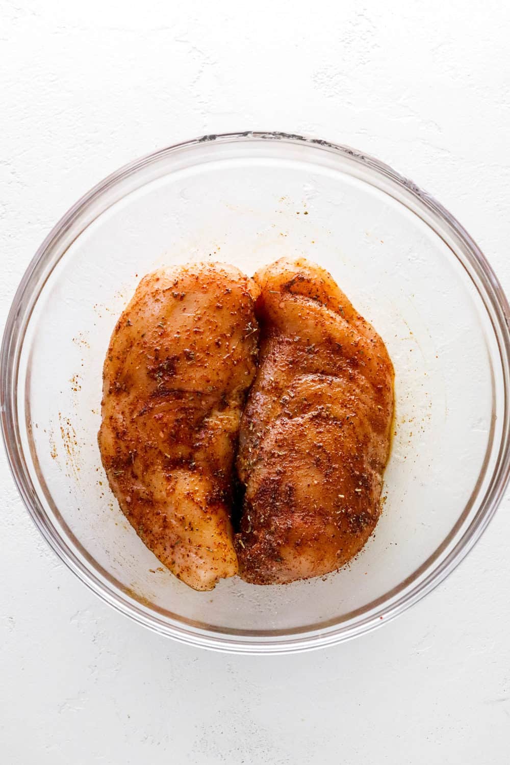Two pieces of chicken breast covered in a spice rub inside a round glass bowl