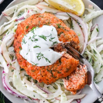 Salmon burger onto pf Cole slaw on a plate with fork cutting through the salmon