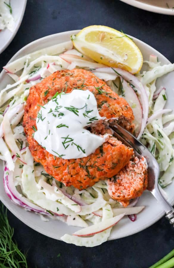 Salmon burger onto pf Cole slaw on a plate with fork cutting through the salmon