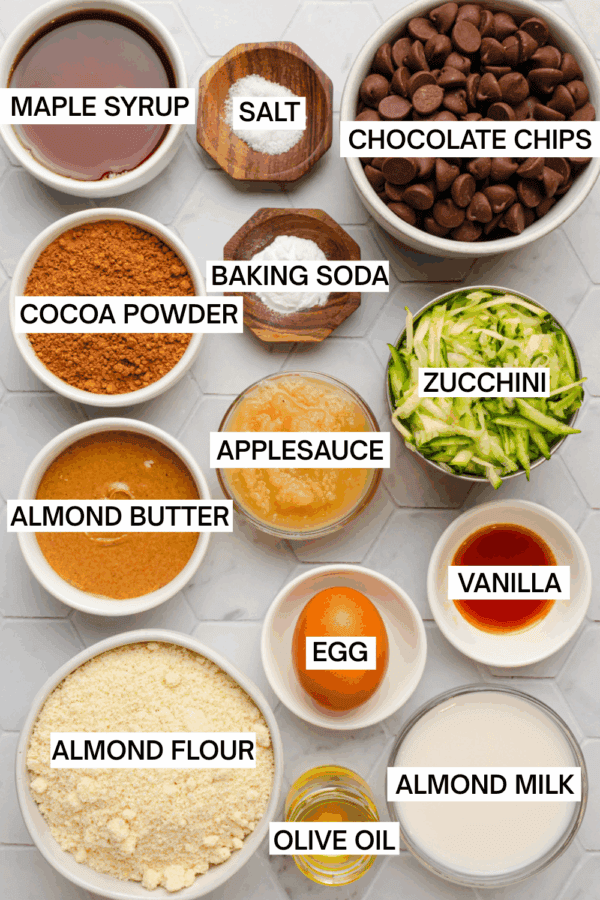 Ingredients for chocolate zucchini muffins in bowls with labels over each ingredient.