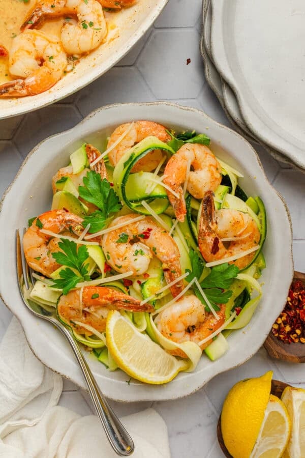 Healthy shrimp scampi in a bowl with more cooked shrimp in a bowl behind it.