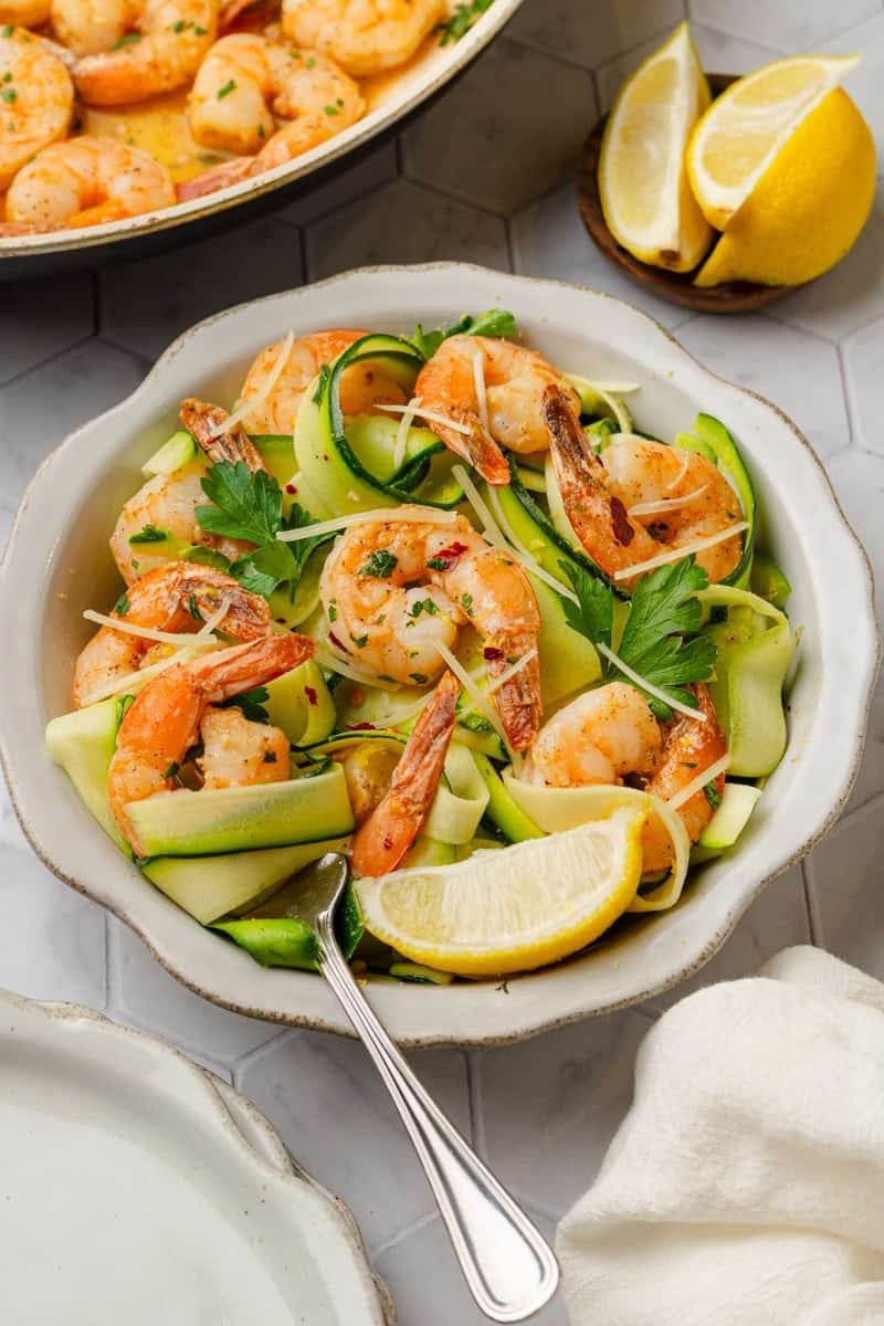 Zucchini noodle shrimp scampi meal in a bowl with more in a pan behind it. 