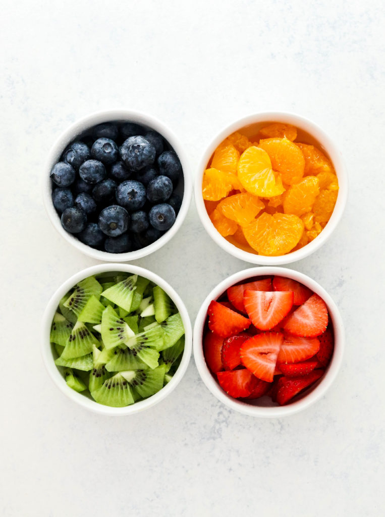 4 small white bowls filled with blueberries, oranges, cut kiwi and sliced strawberries