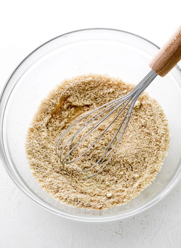 Round glass bowl filled with whisked dry muffin ingredients with a metal whisk in the bowl