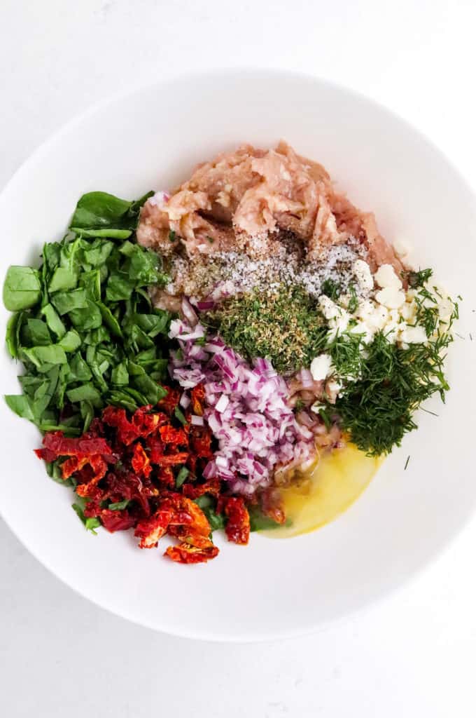 ground chicken, spinach, diced red onion, tomatoes , herbs and spices in a round white mixing bowl