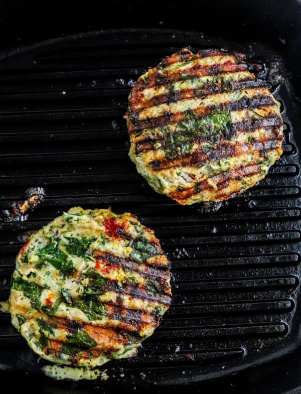 Two chicken burgers being grilled on a black grill pan