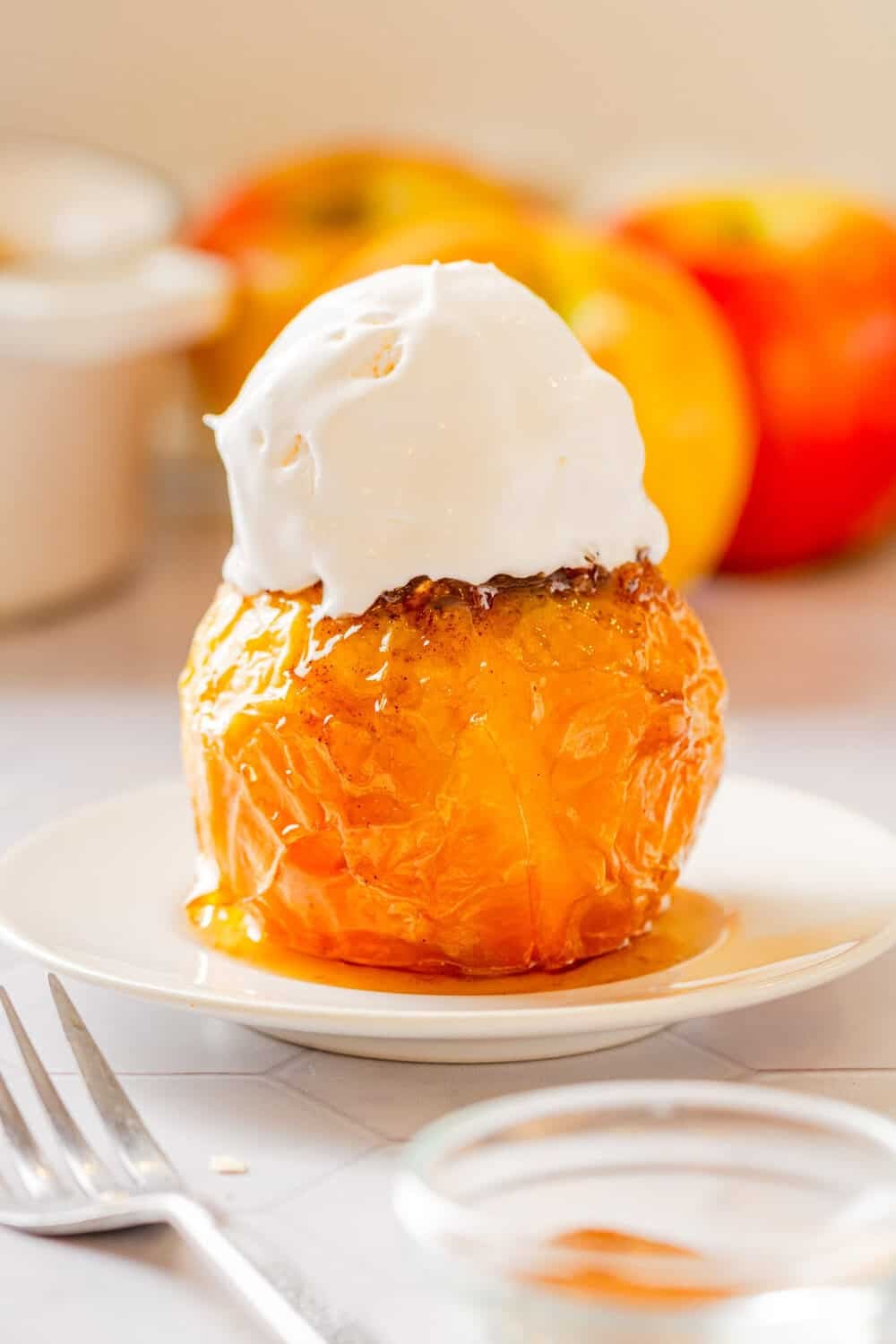 Baked apple cooked in the air fryer with ice cream on it on a plate with more baked apples behind it.