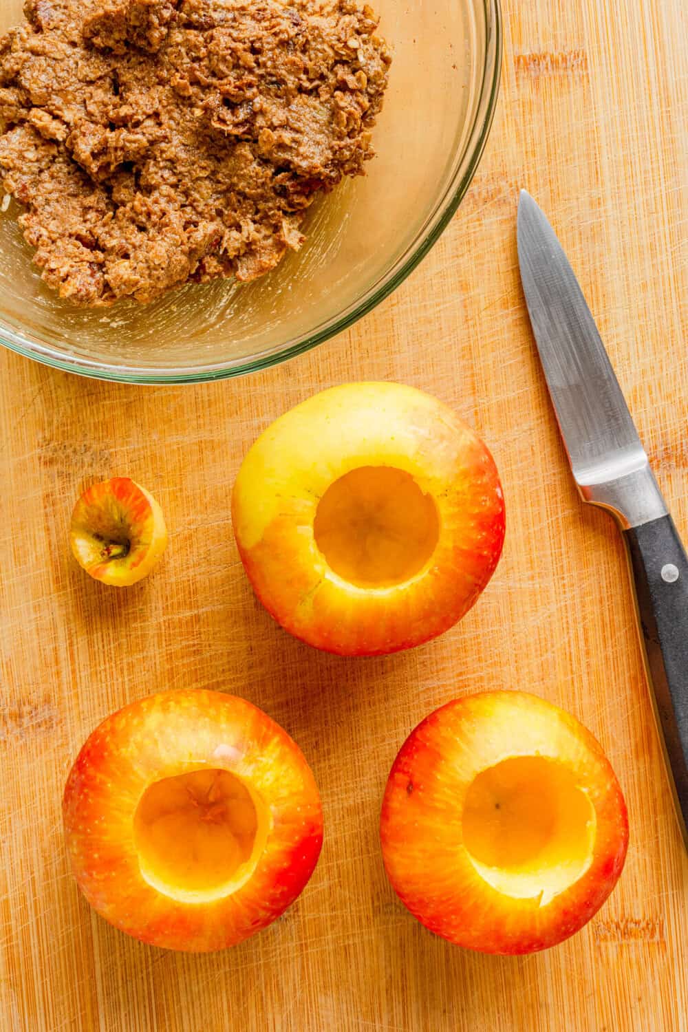 Hollowed out apple on a cutting board with apple filling in a bowl behind it.