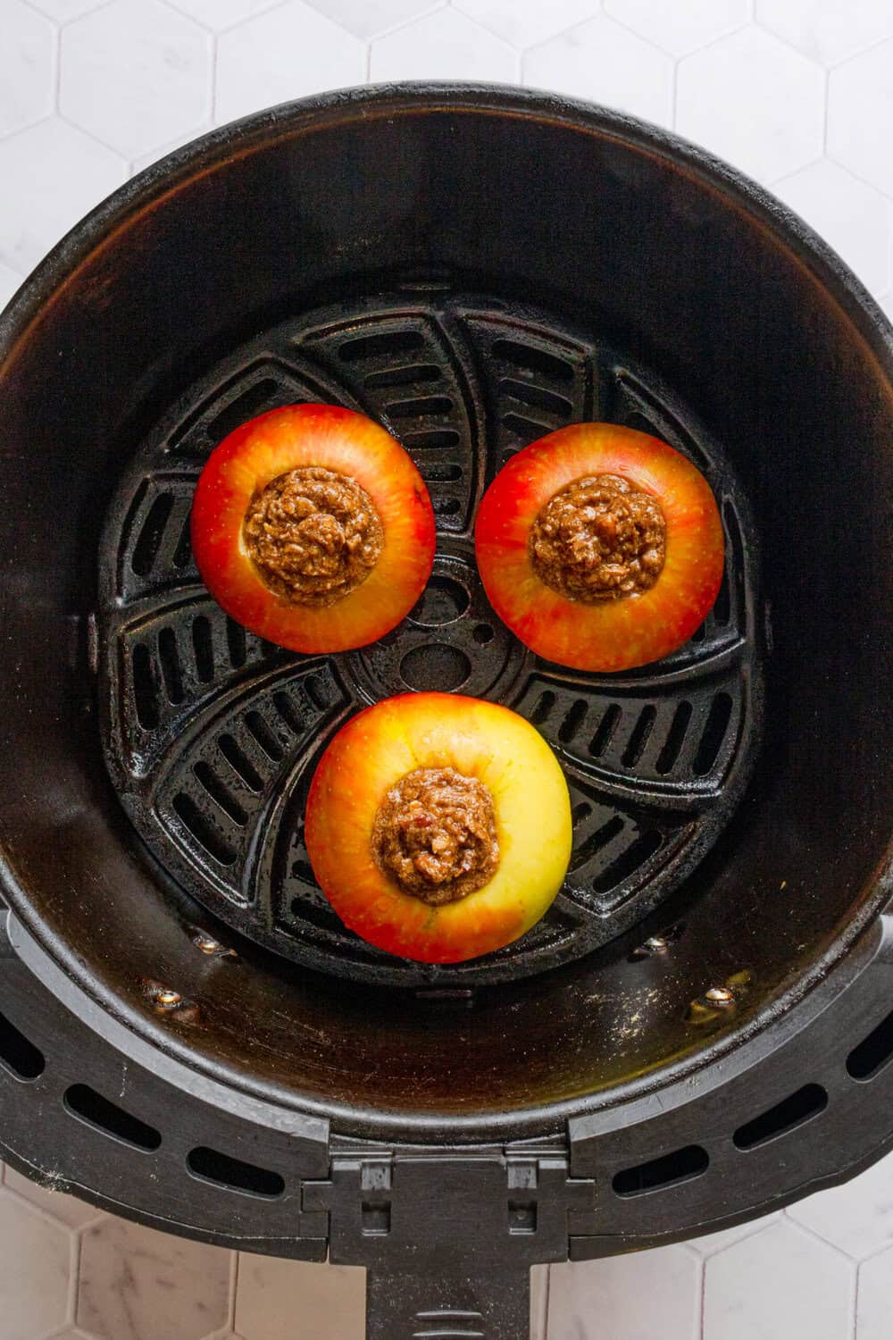 Filled uncooked apples in an air fryer basket.