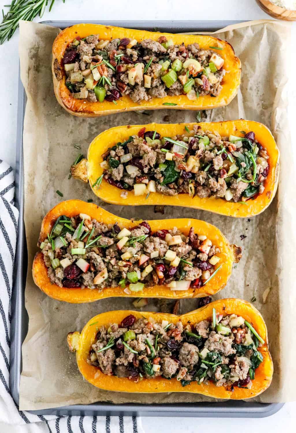4 pieces of cut whole squash filled with sausage and veggies stuffing ontop of brown parchment paper.